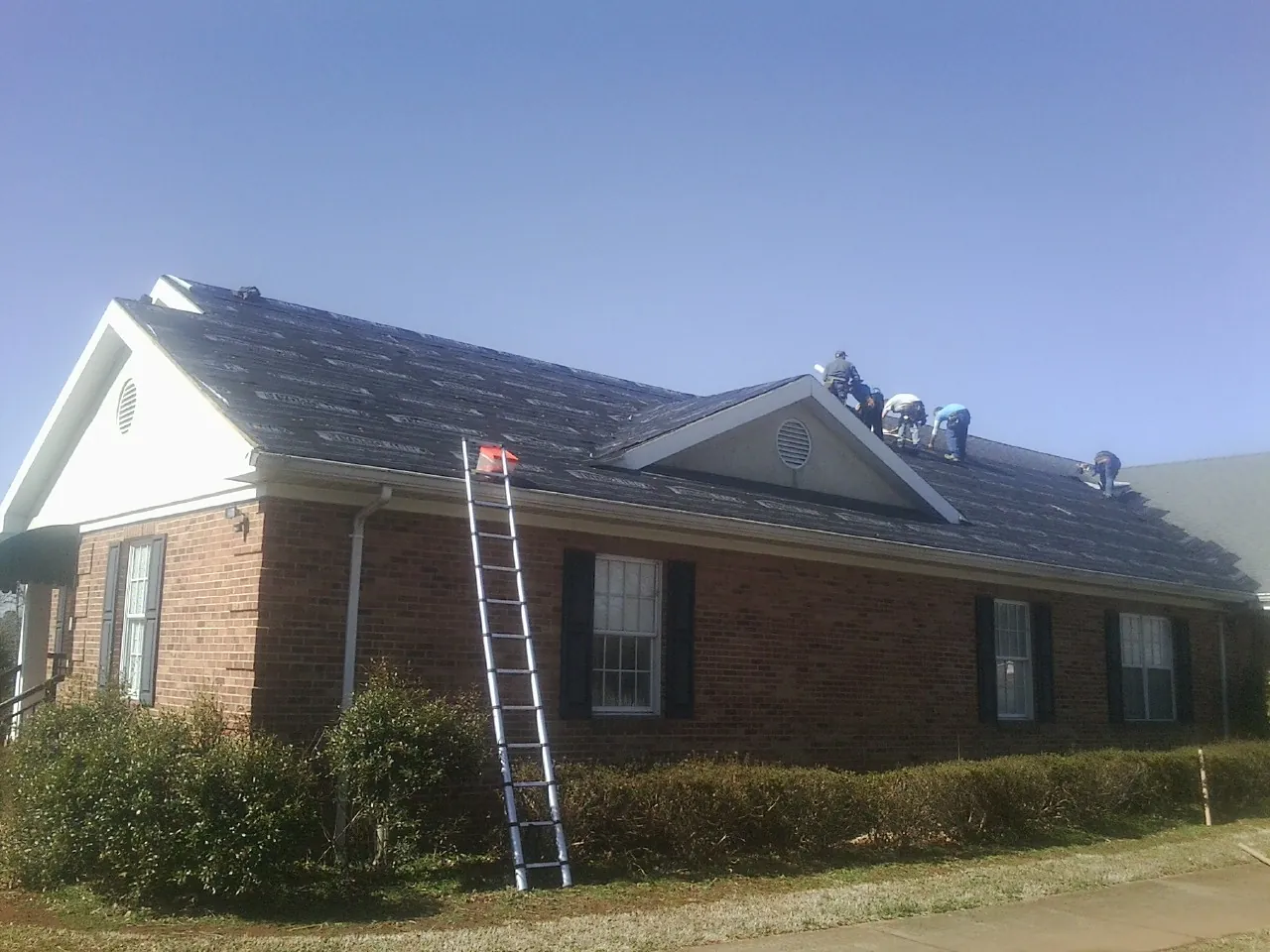 Crew tearing shingles off a brick ranch roof with a ladder set — Emergency Roof Repair work by our crew in Pala