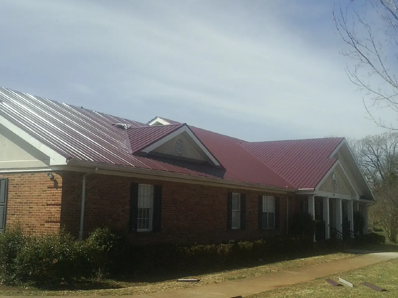 Red metal roof with gabled entries on a long brick building, from a Hail Damage Roof Repair job in Pala