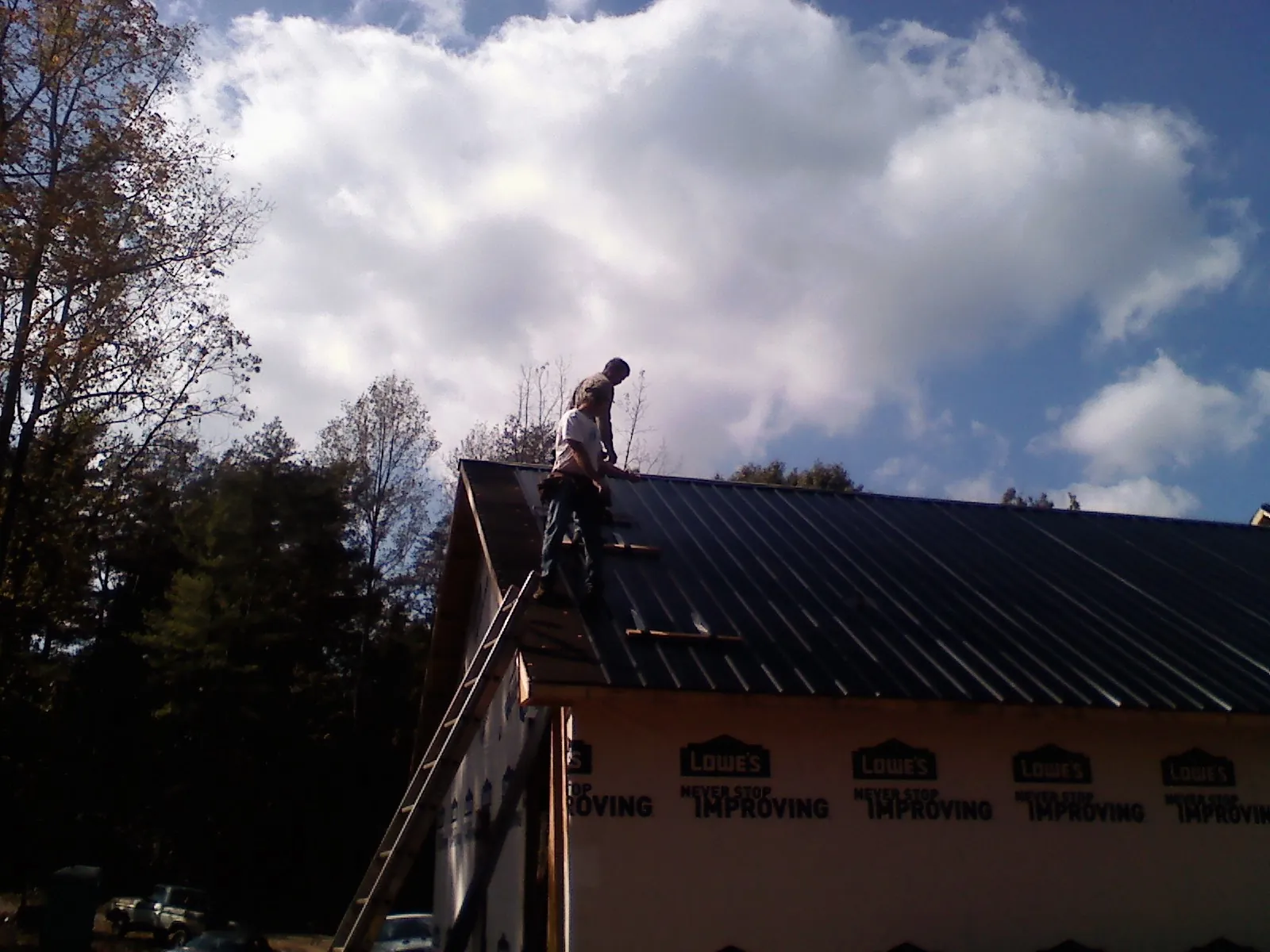 Roofer fastening dark metal panels high against a cloudy sky, from a Roof Inspection job in Pala